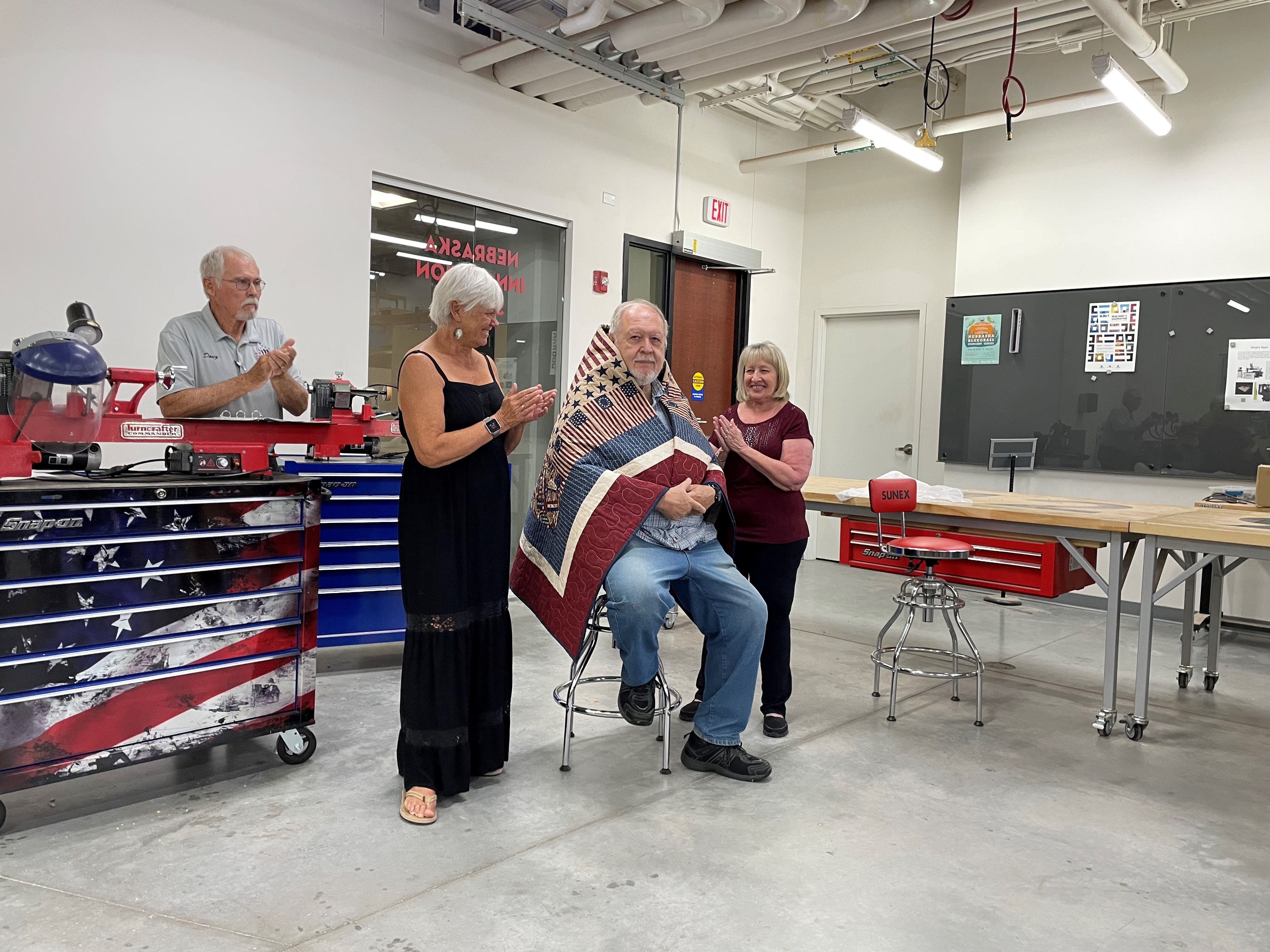 Jim Young (seated) is wrapped in his quilt from the Quilts of Valor Foundation by his sister-in-law, Pat Young, and wife, Victoria, while Doug Kapke of Fairbury looks on. 