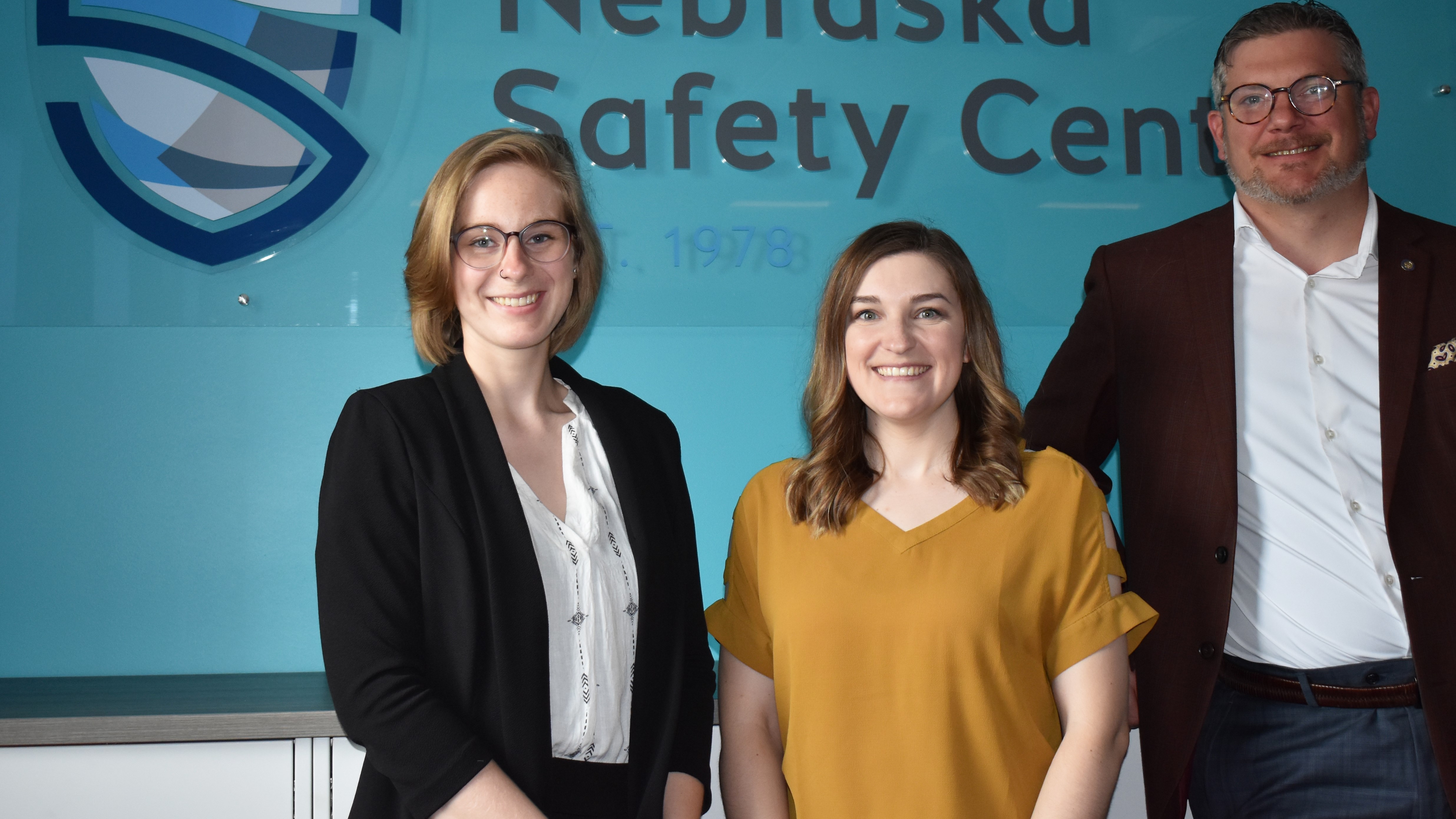 Nebraska Safety Center staff standing in front of a teal wall and logo sign