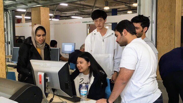 âIt takes a village with Adobe Illustrator.â Students surround a computer during their Innovation Studio class, practicing language skills and gaining hands-on experience for their studies.