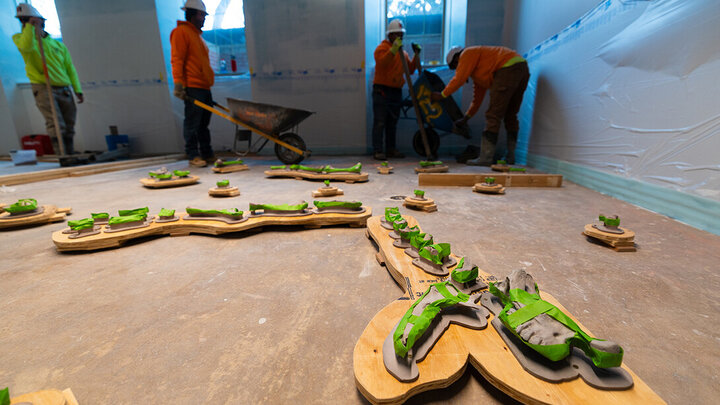 Concrete molds and tools on a floor as workers in safety gear prepare materials nearby.