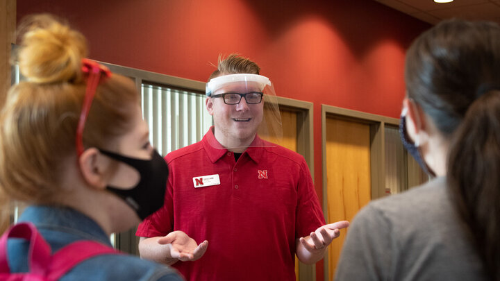 David Strang, an events associate with Academic Services and Enrollment Management, wears a face shield from Nebraska Innovation Campus while visiting with fellow Huskers. The face shields will be distributed to offices and colleges across campus to support students who are deaf or hard of hearing. 