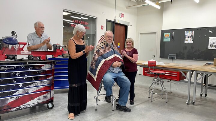 Jim Young (seated) is wrapped in his quilt from the Quilts of Valor Foundation by his sister-in-law, Pat Young, and wife, Victoria, while Doug Kapke of Fairbury looks on. 