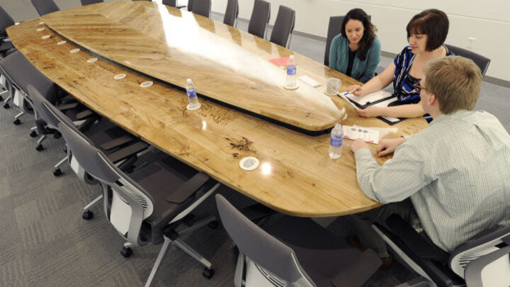 Cheryl Horst (from left), Rose Robotham and Phill Bakken, of NUtech Ventures work Monday at the boardroom table in the Innovation Commons building on Innovation campus. The table was built using green ash from trees cut down at the former State Fair Park.